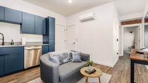 Un appartement moderne doté d’une cuisine, d’un canapé gris, d’une petite table ronde et d’un plancher en bois.
