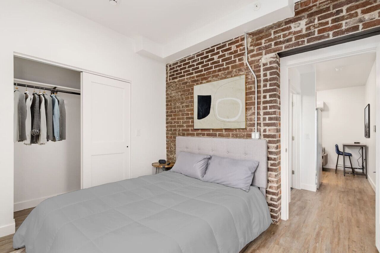 Een slaapkamer met een bed, een kledingkast, een bakstenen muur en een kleine tafel met een stoel.