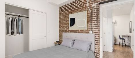 Een slaapkamer met een bed, een kledingkast, een bakstenen muur en een kleine tafel met een stoel.