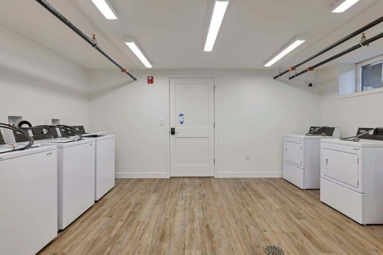 Une buanderie équipée de plusieurs machines à laver, une porte avec une enseigne bleue et un éclairage fluorescent.