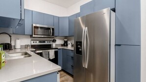 Una cocina moderna con armarios azules, un refrigerador de acero inoxidable, un microondas y una estufa.