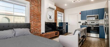 A modern room with a bed, a TV, a fireplace, and a kitchenette.