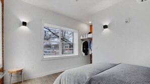 A bedroom with a large window, a bed, a small stool, and a closet with hanging clothes. - Modern Apartment with Pool Table! Pet-friendly! (Columbus)