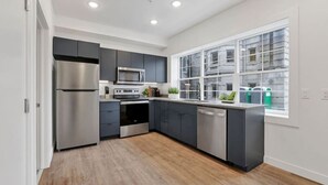 A modern kitchen with stainless steel appliances, grey cabinets, and a large window with a view of a building. - Modern Apartment with Pool Table! Pet-friendly! (Columbus)