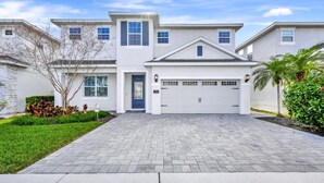 A two-story house with a garage, a front door, and a paved driveway. - Stylish Home near Disney: Themed & Game Room + Waterpark - 300BU (Kissimmee)