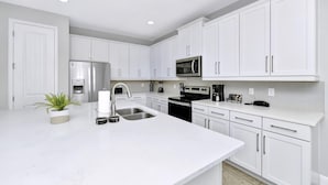 A modern kitchen with white cabinetry, stainless steel appliances, and a central island with a sink. - Stylish Home near Disney: Themed & Game Room + Waterpark - 300BU (Kissimmee)