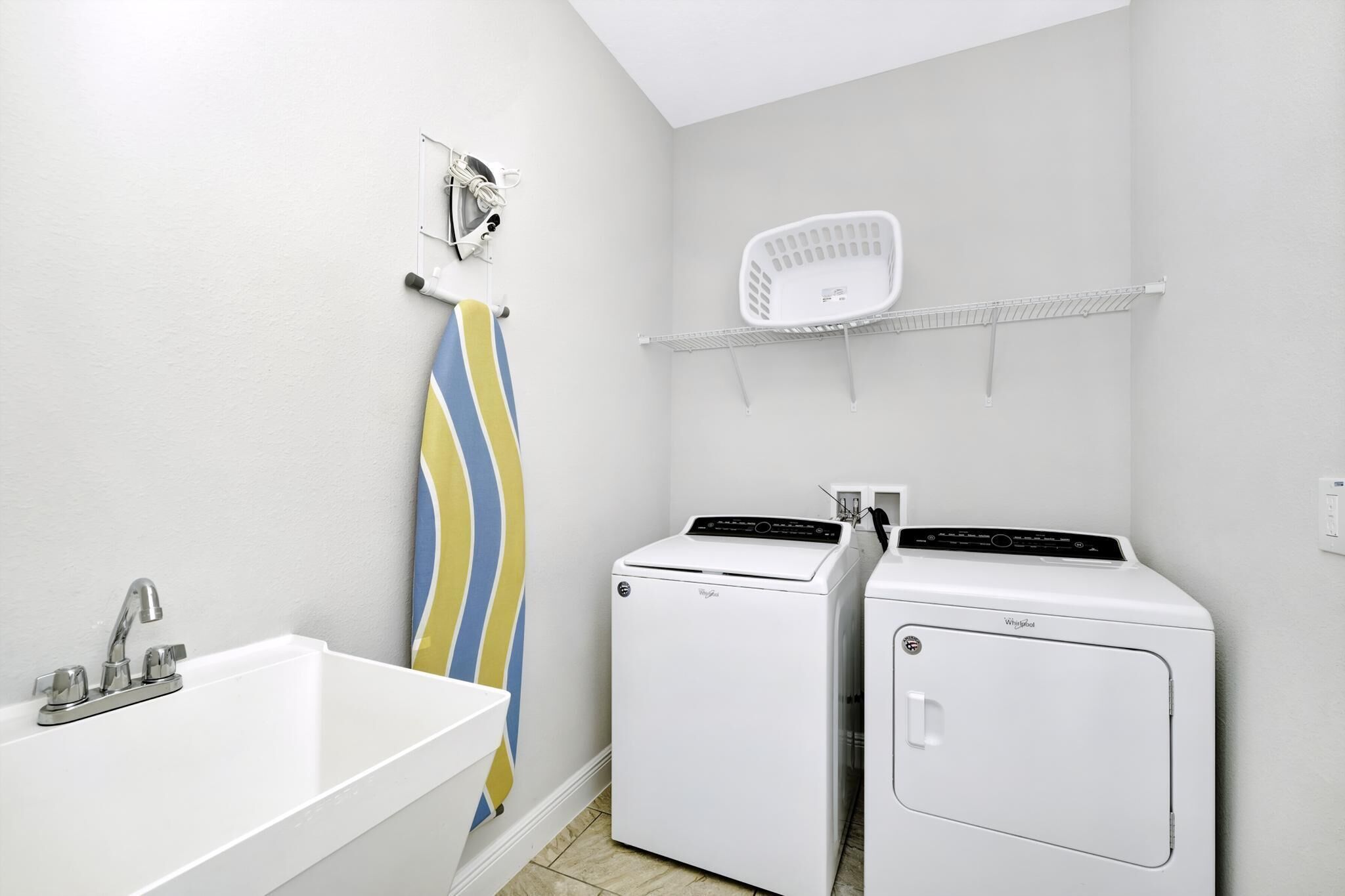 A laundry room with a white sink, two white washing machines, a towel rack, and a laundry basket on a shelf.