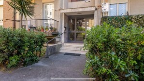 A building entrance with a metal staircase leading to a glass door, surrounded by greenery and potted plants. - Per una vacanza meravigliosa. (La Spezia)