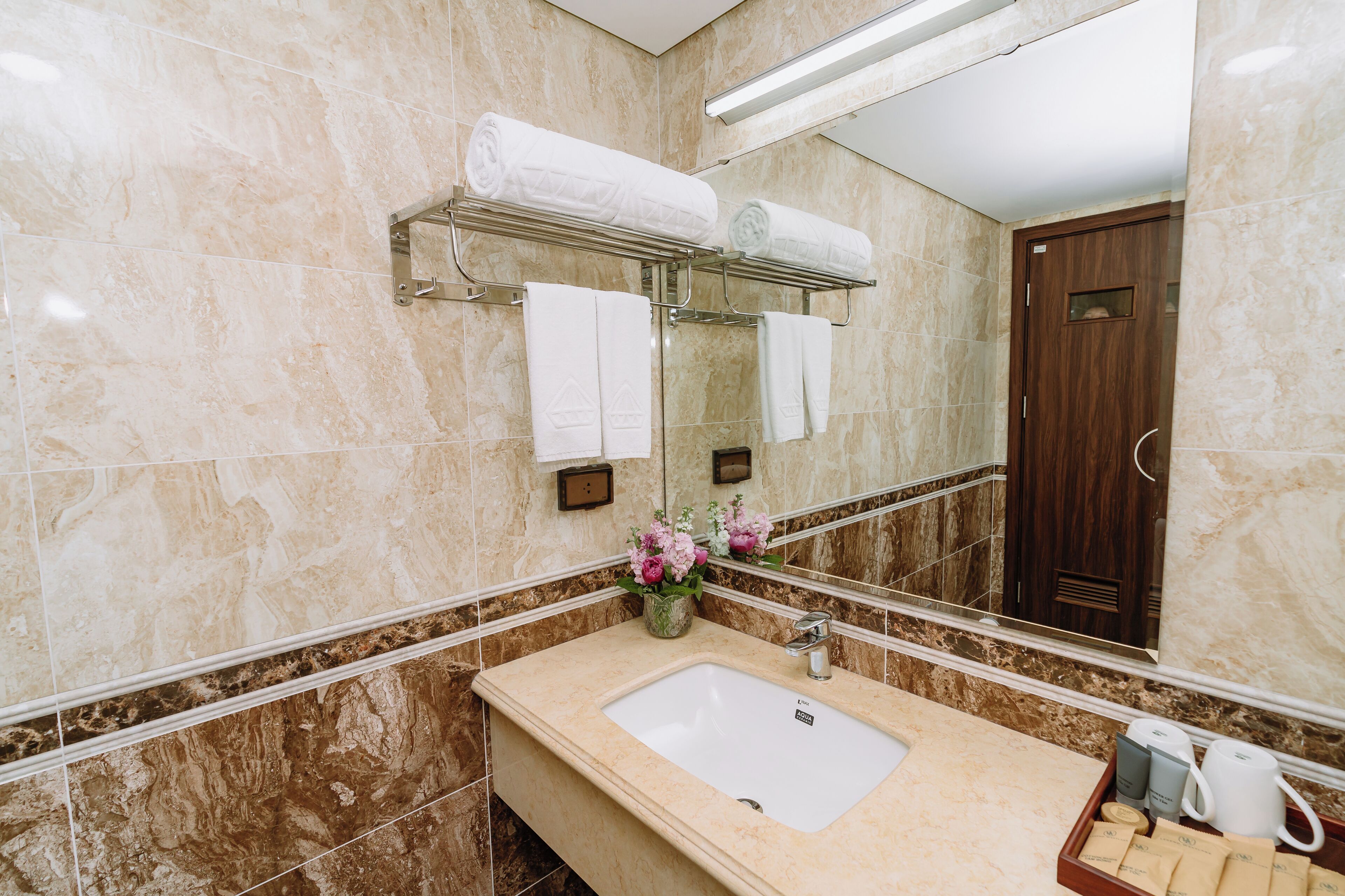 Un baño con lavamanos de mármol, toallero, espejo y puerta de madera.