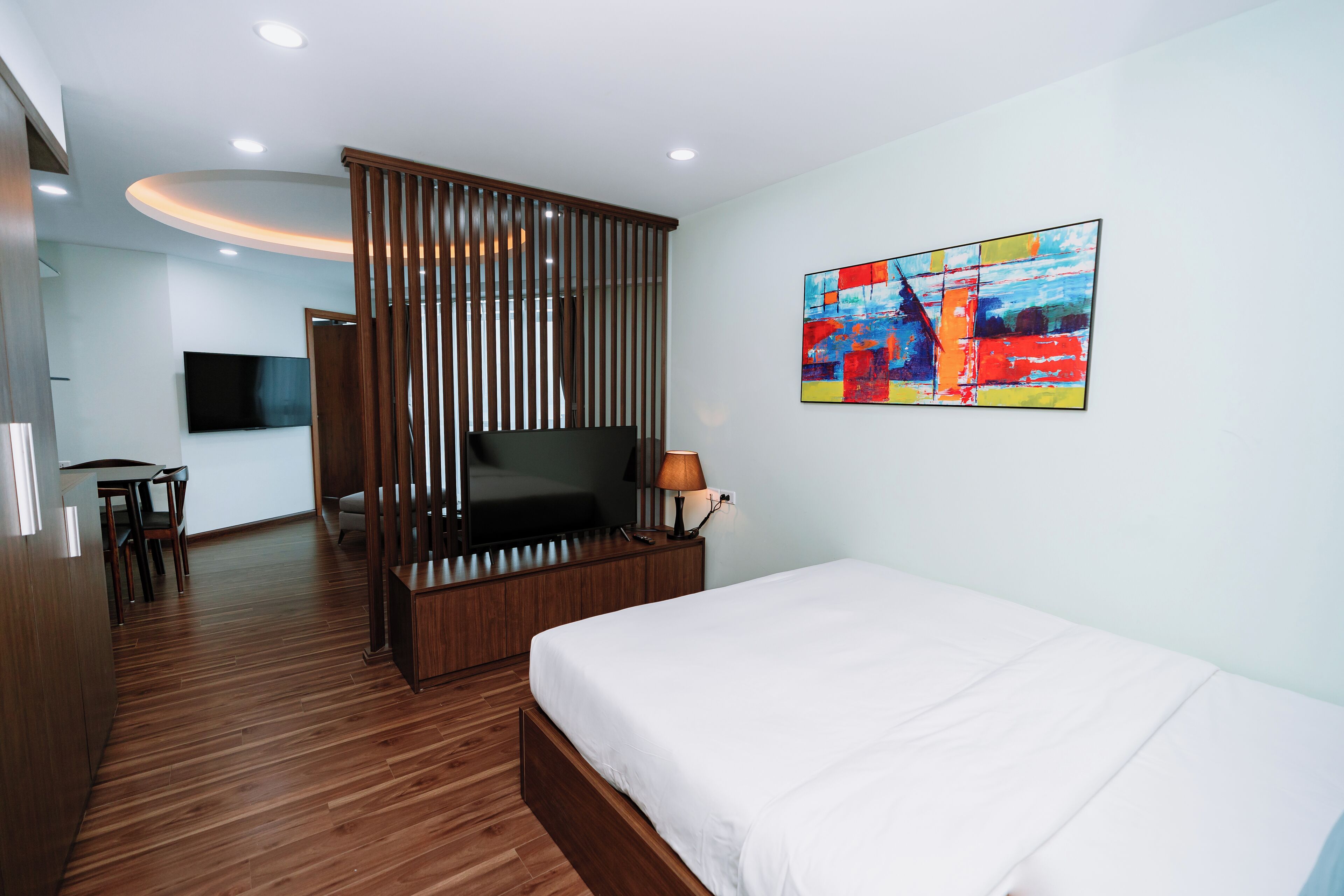 Une chambre d’hôtel moderne avec un plancher en bois, un lit, une télévision, un bureau et une peinture abstraite aux couleurs vives.