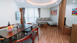 A modern living room with a wooden floor, a dining table with chairs, a sofa, and a TV mounted on the wall. - Legend Westlake Hotel (Hanoi)