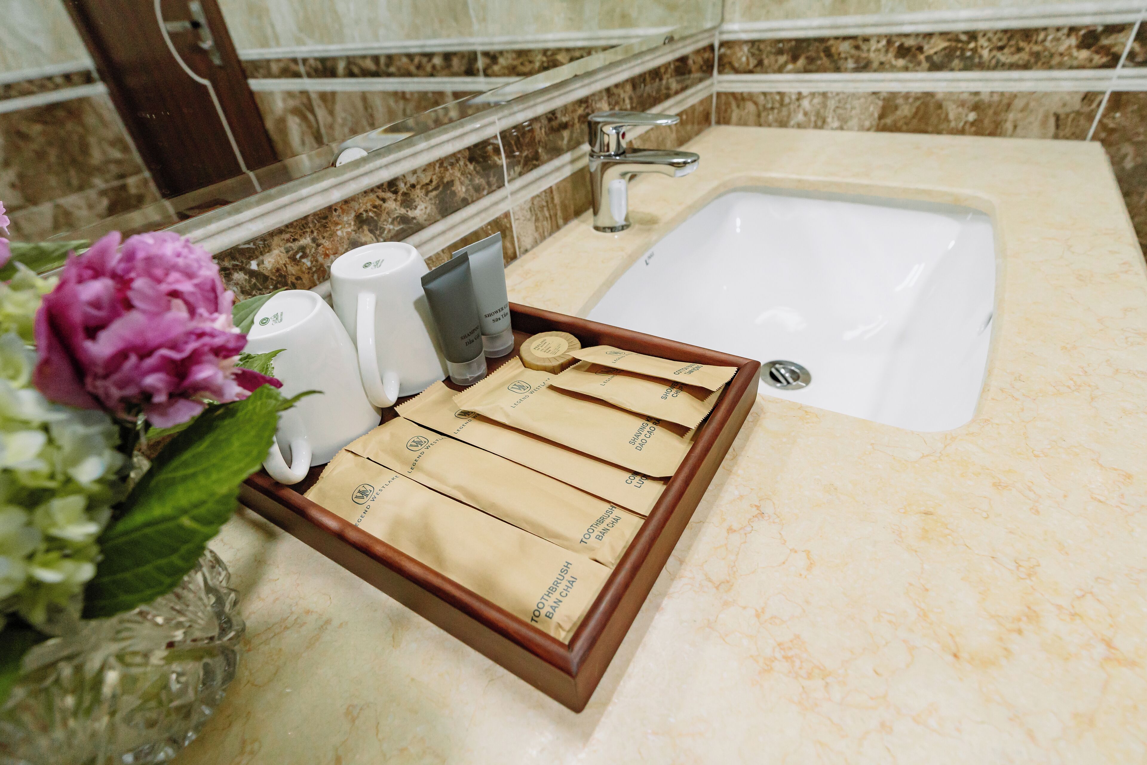 Un baño con encimera de mármol, un lavabo blanco y una bandeja con artículos de aseo.