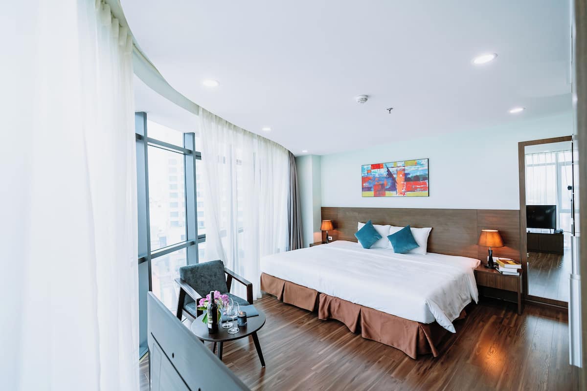 Habitació d'hotel moderna amb un llit gran, una taula de treball, una cadira i vista a la ciutat.