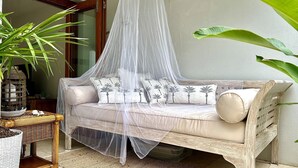 Ein gepolstertes Outdoor-Sofa mit Baldachin, umgeben von tropischen Pflanzen und einem Korbtisch.