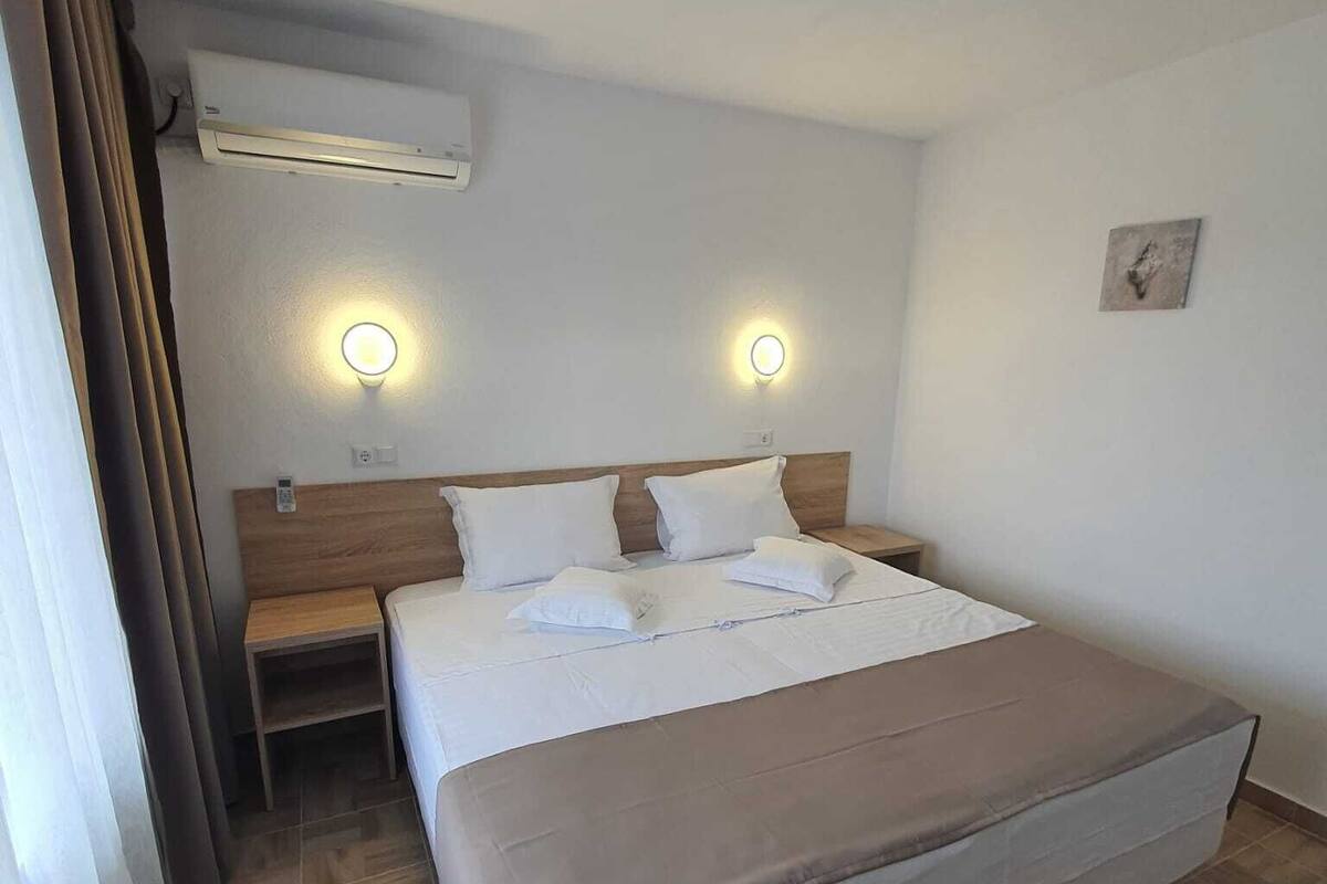 A hotel room with a large bed, two bedside tables, an air conditioning unit, and two wall-mounted light fixtures.
