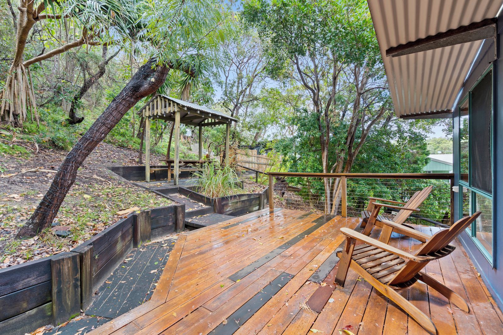 A wooden deck with a wooden chair, surrounded by trees and a covered area.