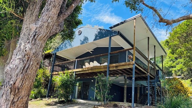 Une maison moderne à deux étages, dotée d’un espace extérieur couvert et entourée d’arbres et de végétation.