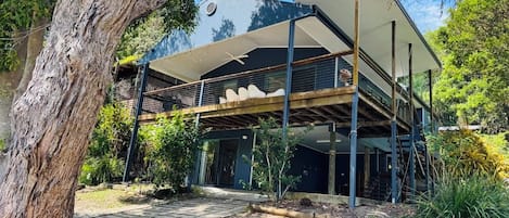 Ein modernes, zweistöckiges Haus mit überdachter Terrasse, umgeben von Bäumen und Grünpflanzen.