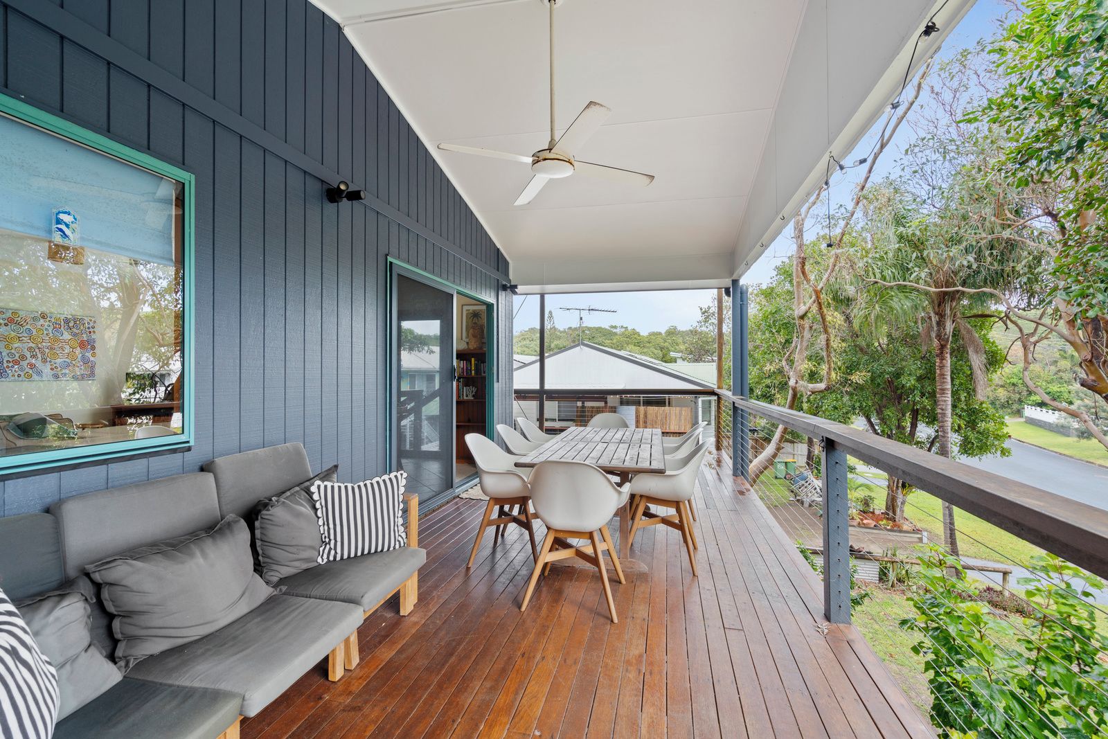 A covered outdoor seating area with a wooden deck, a sofa, and a table with chairs.