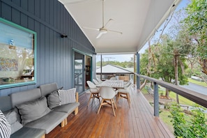 A covered outdoor seating area with a wooden deck, a sofa, and a table with chairs.