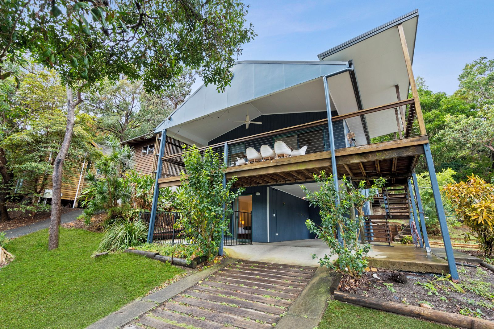 Una casa moderna de dos pisos con un espacio exterior cubierto, una escalera y un jardín.