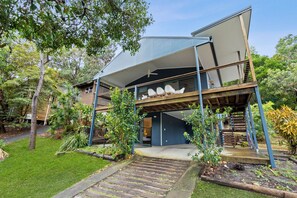 A modern two-story house with a covered outdoor area, a staircase, and a garden.