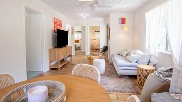 Ein modernes Wohnzimmer mit Sofa, Fernseher auf einem Holzboden und einem Essbereich mit Tisch und Stühlen.