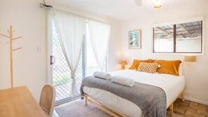 Ein Schlafzimmer mit Bett, Stuhl, Schreibtisch, Fenster und Deckenventilator.