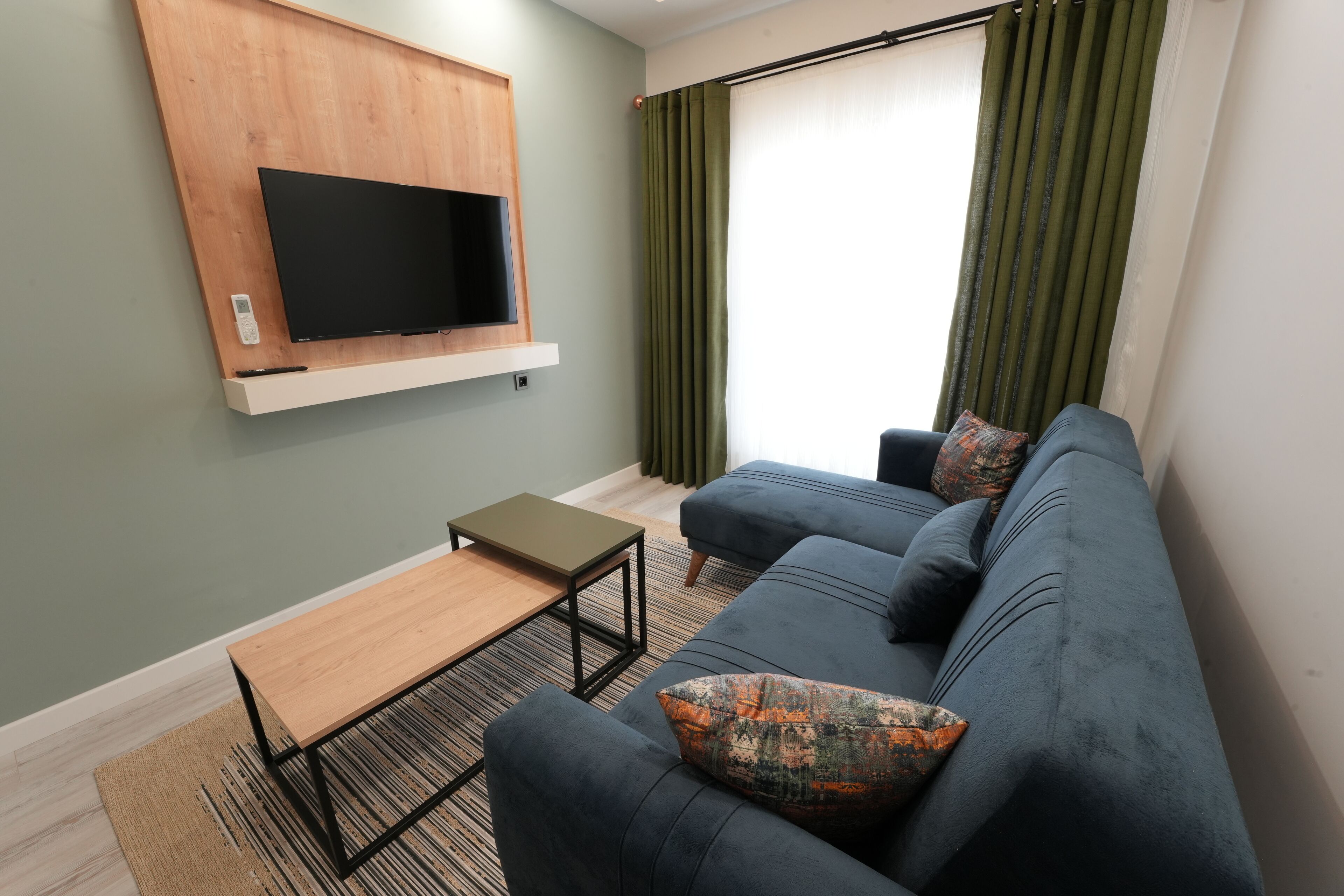 A modern living room with a dark blue sofa, a wooden TV stand, and a small wooden table.