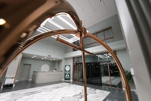 Uma área de recepção de hotel com design moderno, apresentando um balcão de atendimento, uma grande porta de vidro de entrada e piso de mármore.