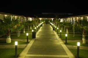 Um caminho iluminado por luzes uniformemente espaçadas, levando a um edifício com várias divisões.