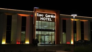 Exterior del Hotel Expo Garden, con un letrero llamativo, amplias ventanas y una entrada bien iluminada.