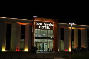 Exterior do Expo Garden Hotel, com placa visível, grandes janelas e entrada bem iluminada.