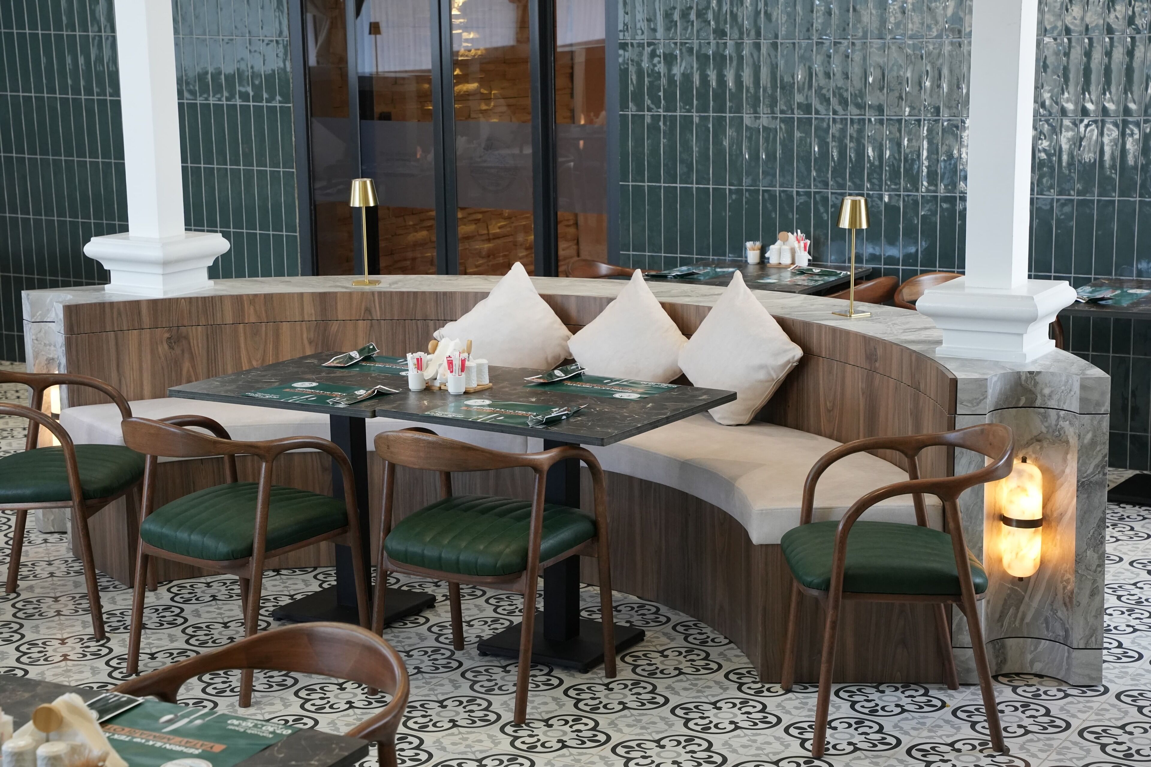 Un restaurante con una zona de estar curva, sillas acolchadas verdes y una barra de mármol.