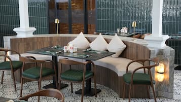Un restaurante con una zona de estar curva, sillas acolchadas verdes y una barra de mármol.