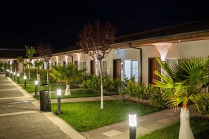 Um corredor de hotel com caminhos iluminados, plantas em vasos e um gramado bem cuidado.