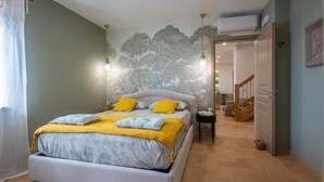 Une chambre à coucher comprenant un lit, une table de chevet, une fresque murale et un escalier menant à une autre pièce.