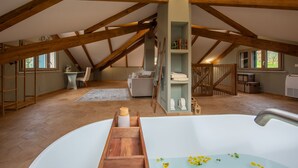 Une chambre spacieuse située sous les combles, dotée d’une grande baignoire, de poutres apparentes, d’un lit en mezzanine et d’un coin salon confortable.