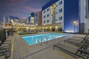 Un hotel con piscina, zona de estar al aire libre y un edificio de varios pisos con habitaciones de diferentes colores.