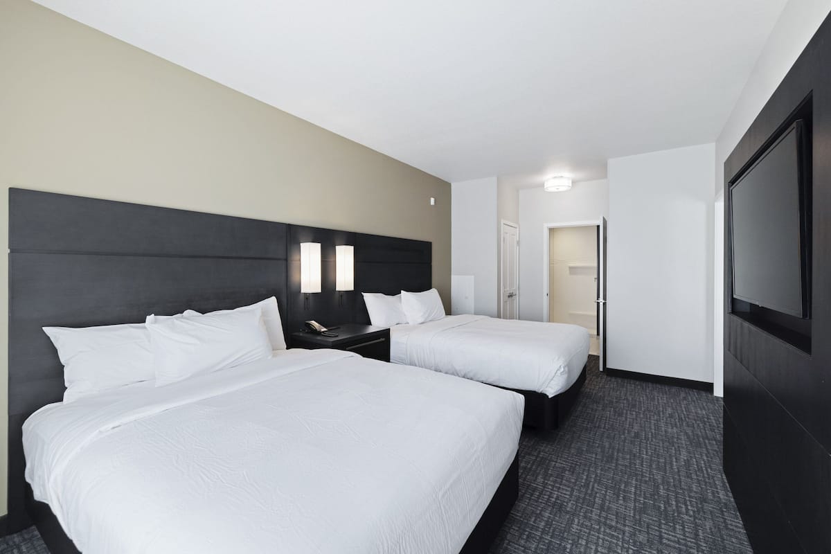 A hotel room with two beds, a dark headboard, a flat-screen TV, and a door leading to another room.