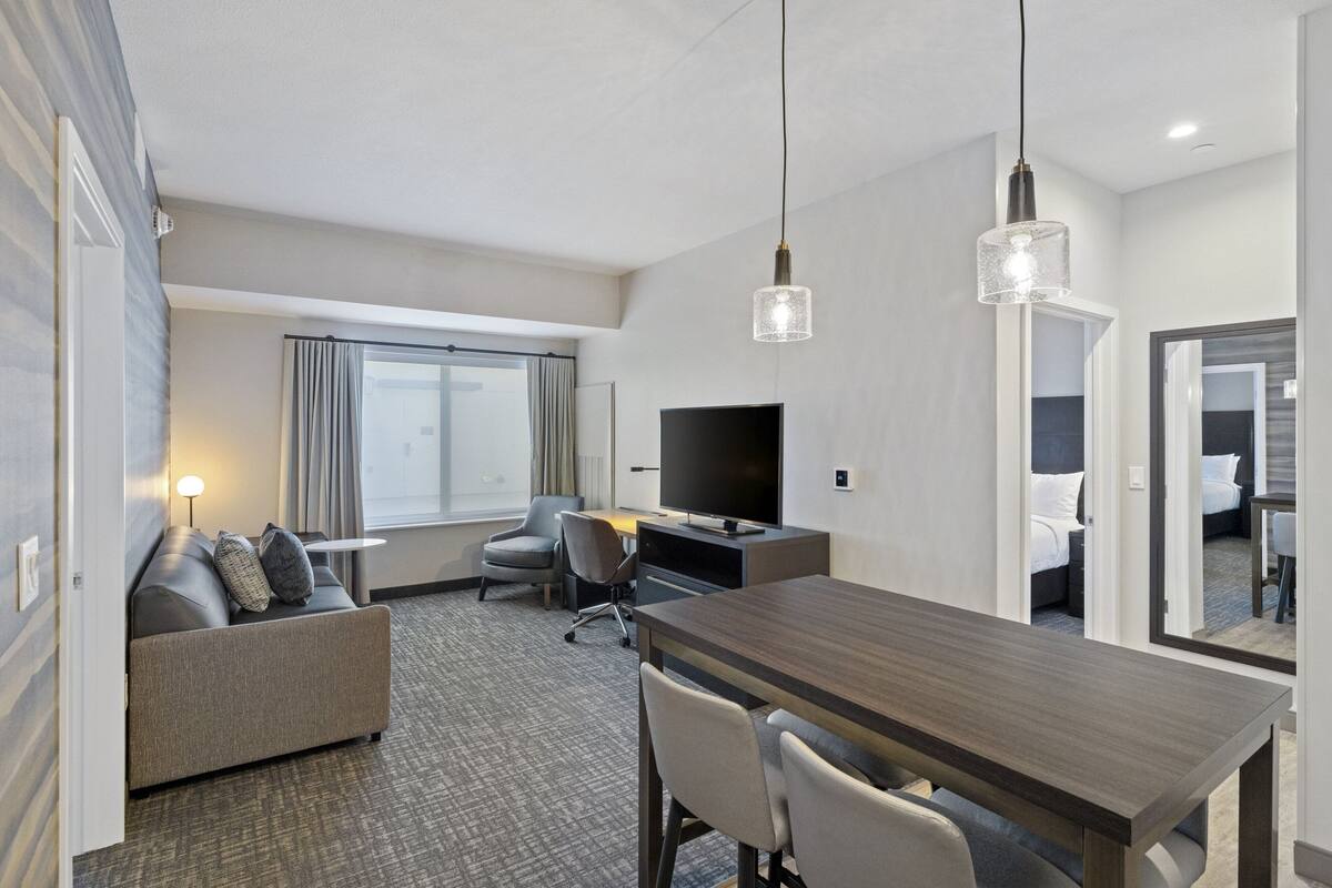 A hotel room with a sofa, a desk, a television, and a dining table.