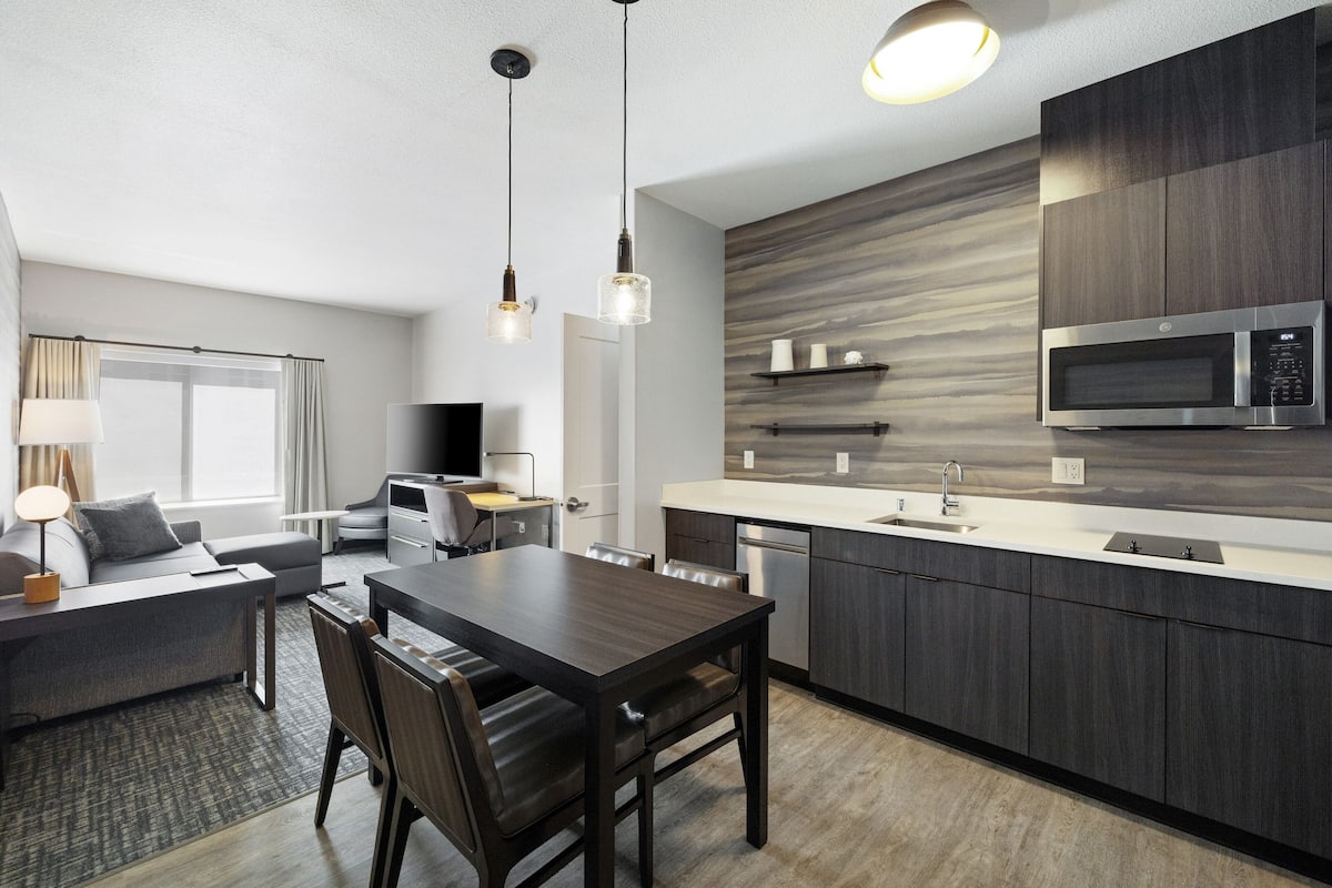 A modern kitchen with dark cabinetry, a built-in microwave, and a dining area with a table and chairs.