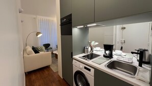 A compact kitchen with a washing machine, a coffee maker, and a sink. - Standing - Place des Vosges - Chambre au Calme (Paris)