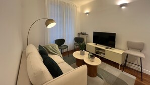 A modern living room with a sofa, two chairs, a coffee table, a TV, and a floor lamp. - Standing - Place des Vosges - Chambre au Calme (Paris)
