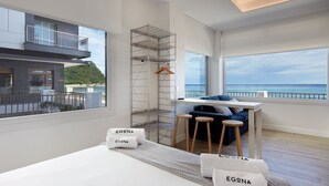 Een moderne hotelkamer met een balkon, een bed met handdoeken, een bureau en uitzicht op zee.