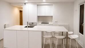 A modern kitchen with white cabinetry, a central island with stools, and a built-in oven.