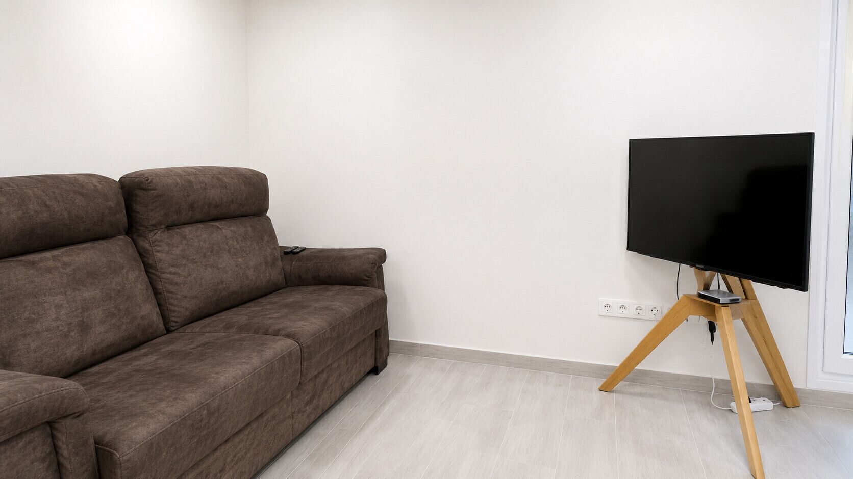 Un salon moderne avec un canapé marron, un téléviseur à écran plat posé sur un meuble en bois et un plancher de couleur claire.