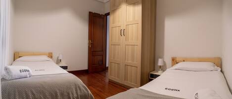 A hotel room with two beds, wooden wardrobe, and a door leading to another room.