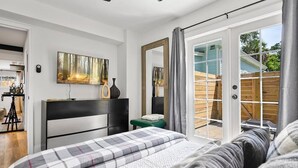 A bedroom with a bed, a desk, a chair, a mirror, and a sliding glass door leading to an outdoor area. - Renovated Bungalow with Work Space, Kitchen, Patio (St. Augustine)