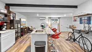A modern kitchen with a central island, bar stools, a bicycle, and a dining area with a view. - Renovated Bungalow with Work Space, Kitchen, Patio (St. Augustine)